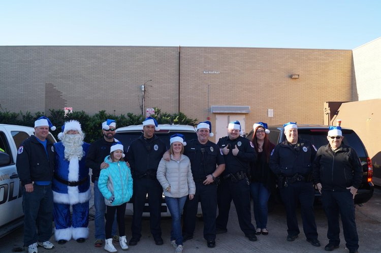 Blue Santa, volunteers, and uniformed officers gather beside police vehicles