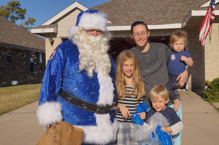 Blue Santa poses with a family outside a home