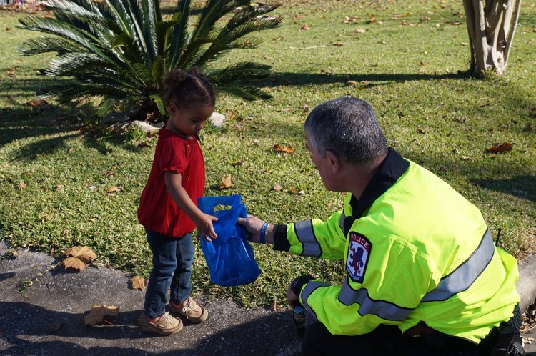 A volunteer in a bright yellow jacket offers a blue gift bag to a child
